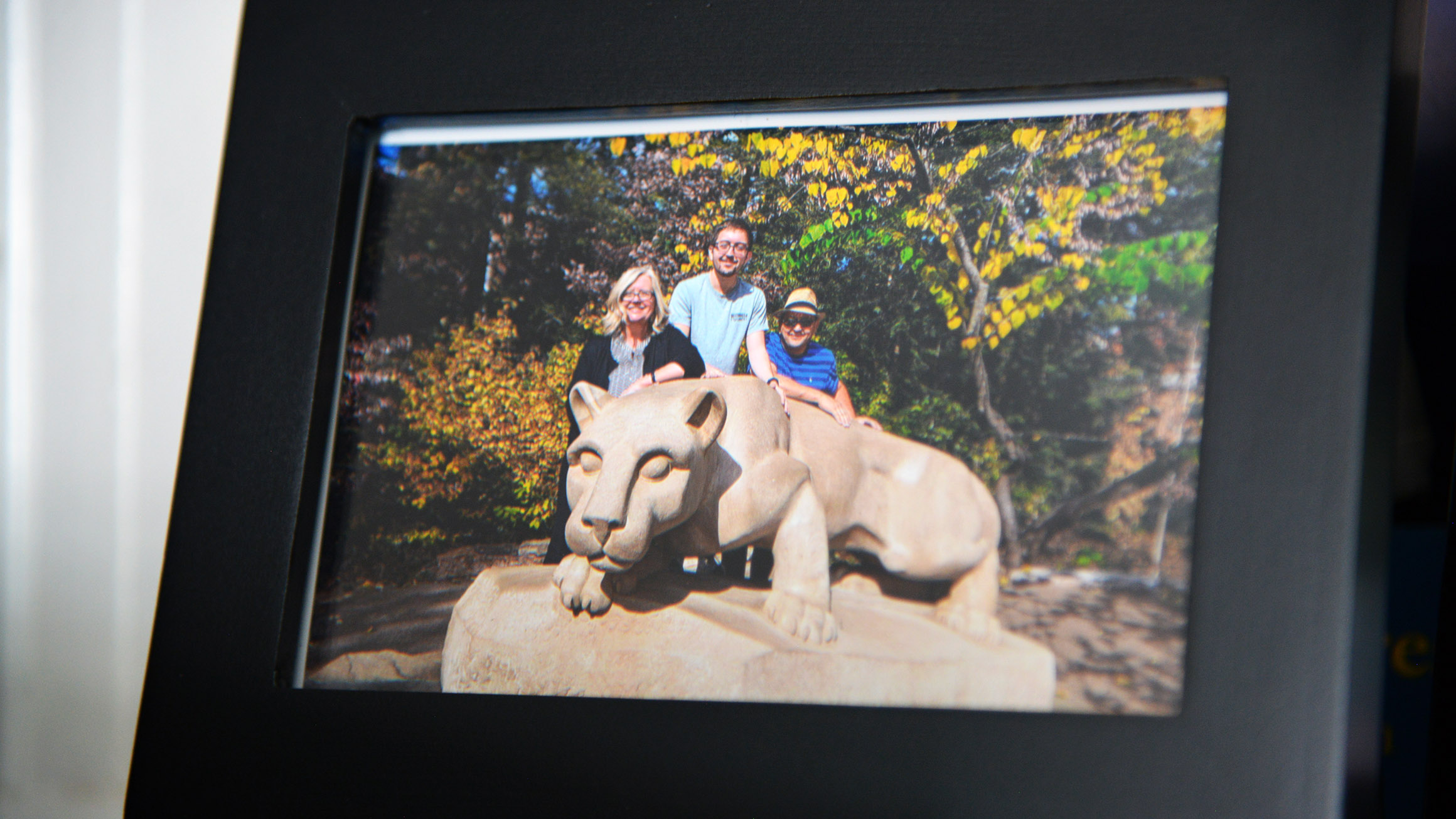 a photo frame shows a picture of a three people standing behind the nittany lion shrine statue