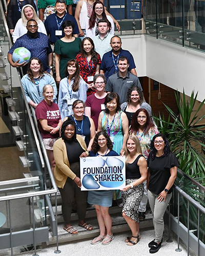 A group of people holding a sign pose on a staircase for a photo.