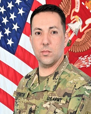 A headshot of a man wearing a military uniform in front of flags.