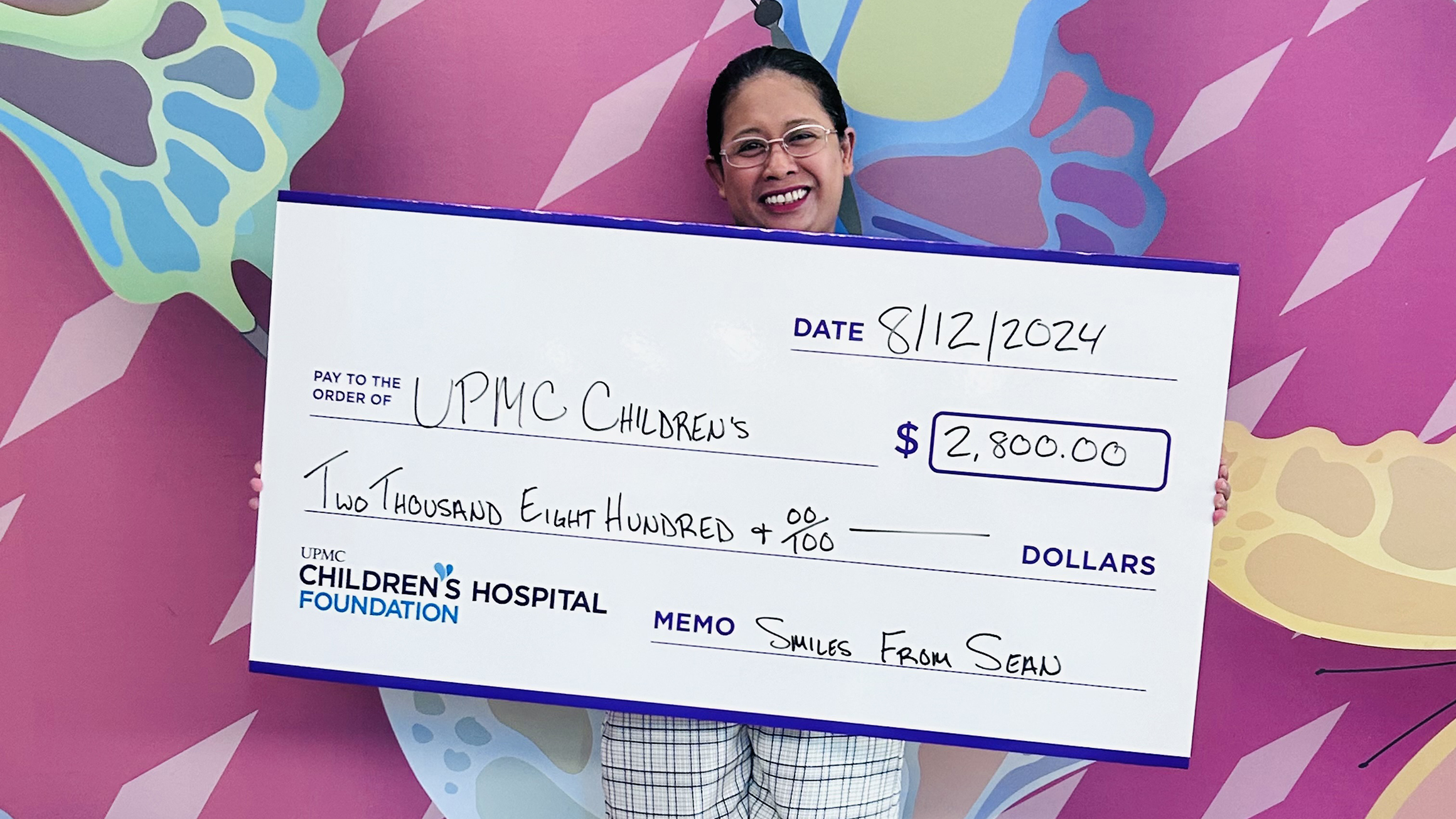 A woman stands in front of a colorful wall with a decorative check.