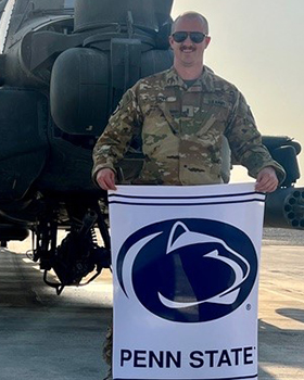 A man wearing a military uniform holding a Penn State flag.