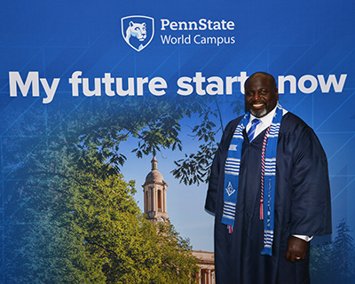 A man wearing a blue graduation gown stands in front of a blue background.