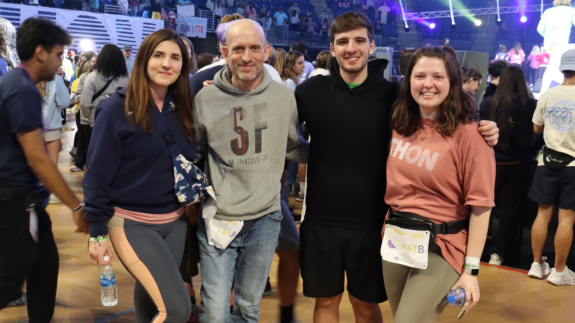 Four people pose in a crowded arena.