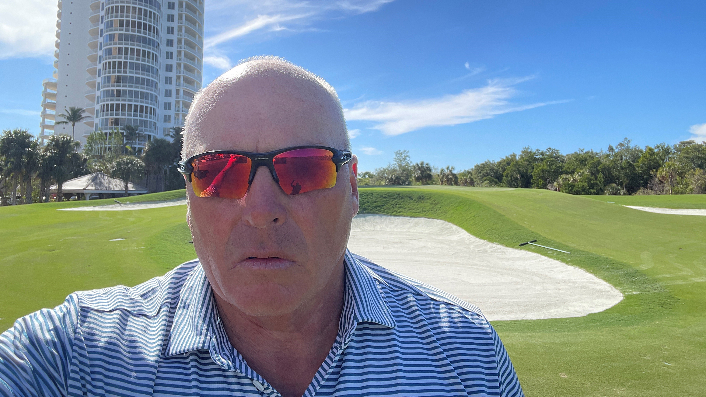 A man wearing sunglasses takes a selfie on a golf course.