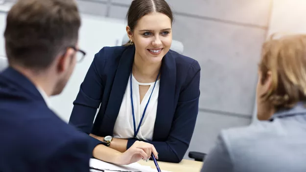 A woman reviewing documents with two peers in a business meeting