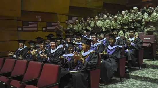 A crowd of soldiers applauds the fellows sitting in an auditorium