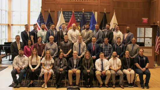 A group of people pose in front of a series of flags.