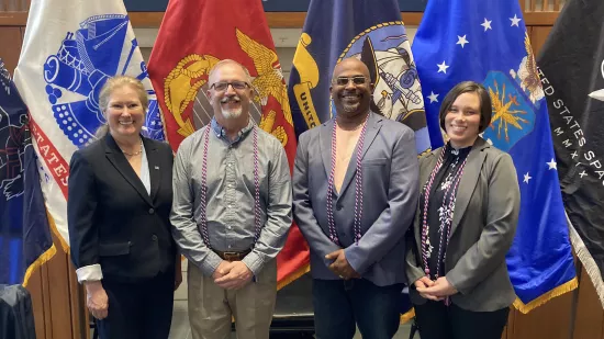 Four people pose in front of a series of flags.