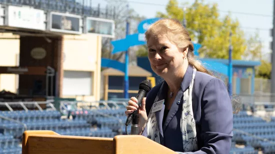 A woman stands at a podium and speaks to an audience.