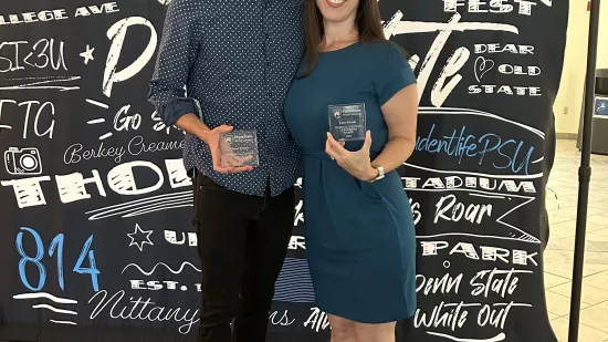 Daniel Serfass stands next to Lauri Accardi, and they are holding award plaques they received.