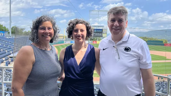 Renee Dorer stands between her mother and father with the infield of a baseball stadium in the background