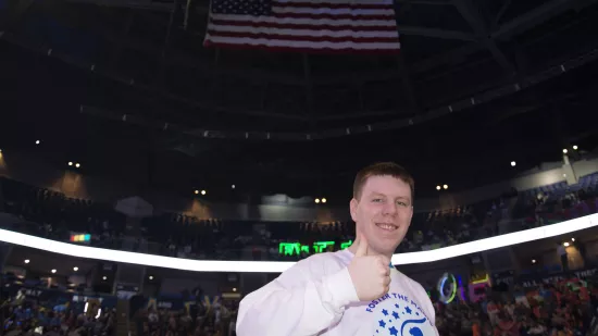 A man holds a "thumbs up" in an indoor arena.