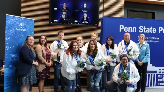 A group of people pose in front of a Penn State background.