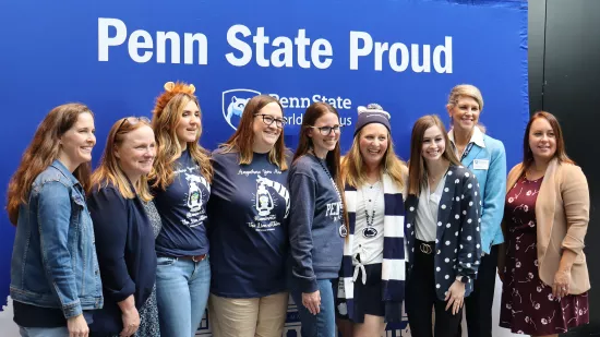 A group of people pose in front of a Penn State background.