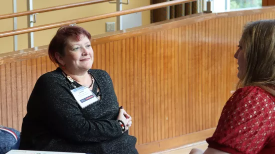 Two women seated at a table have a conversation.