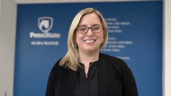 Laura Glotzach stands with the Penn State logo and the alma mater written out on a wall behind her