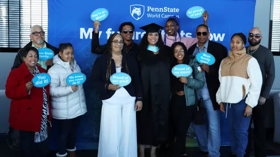 A group of people pose in front of a Penn State background.