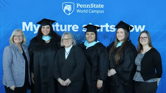 A group of people pose in front of a Penn State background.