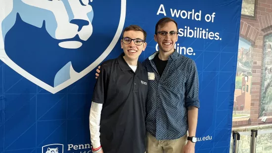 Two men stand shoulder to shoulder in front of a banner with the World Campus logo.