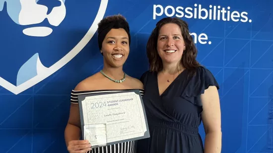 A student holding a plaque stands next to her professor, smiling.