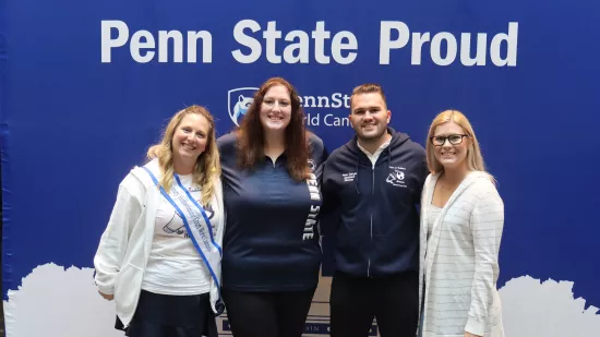 Four people pose in front of a Penn State background.