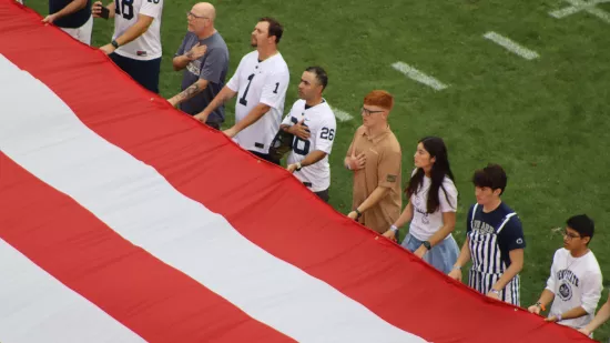 A group of people hold onto a large American flag.