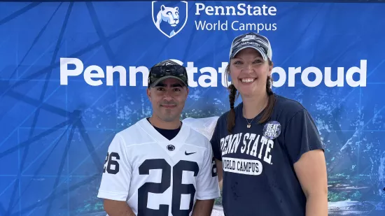 Two people pose in front of a Penn State-themed background.