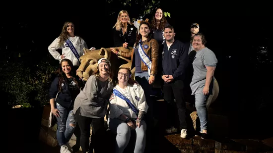 A group of people pose around the Nittany Lion Shrine at night.