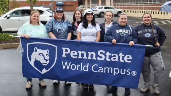 A group of people pose with a Penn State World Campus banner.