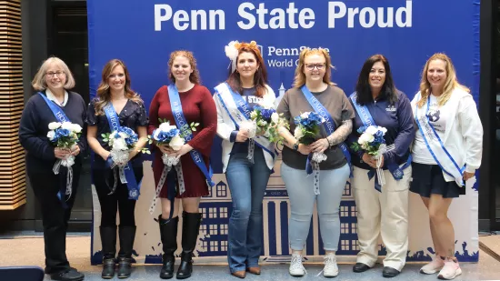 A group of people pose in front of a Penn State background.