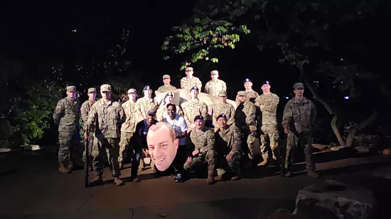 A group of people in camouflaged military uniforms pose with a large cutout of Devon Love's face at the Nittany Lion Shrine.