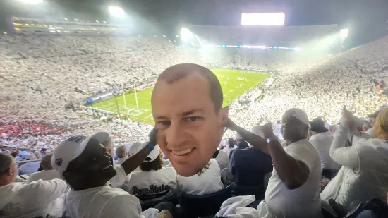 Two men pose with a large cutout of a man's face inside Beaver Stadium.