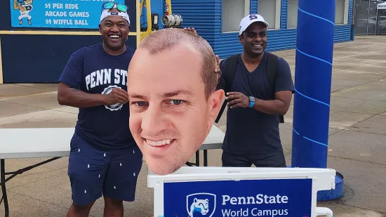 Two men pose with a large cutout of a man's face next to a blue sign.