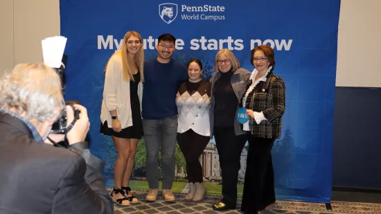 A group of people pose in front of a Penn State background.