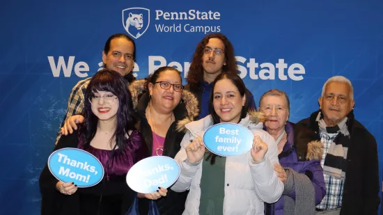 A group of people pose in front of a Penn State background.