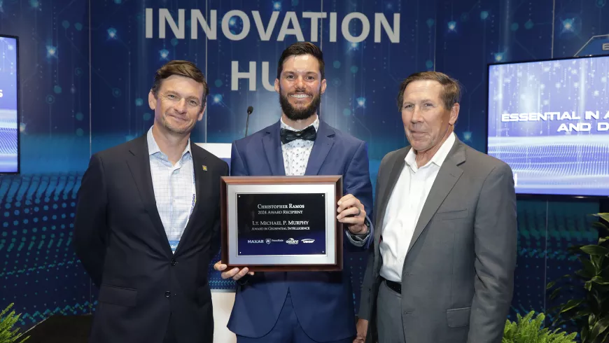 Three men pose for a photo, one holding a plaque.