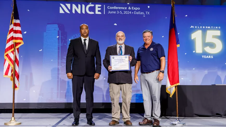 Three people pose with a certificate on a conference stage.